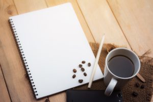 Notebook and coffee cup, with coffee beans inexplicably scattered upon notebook